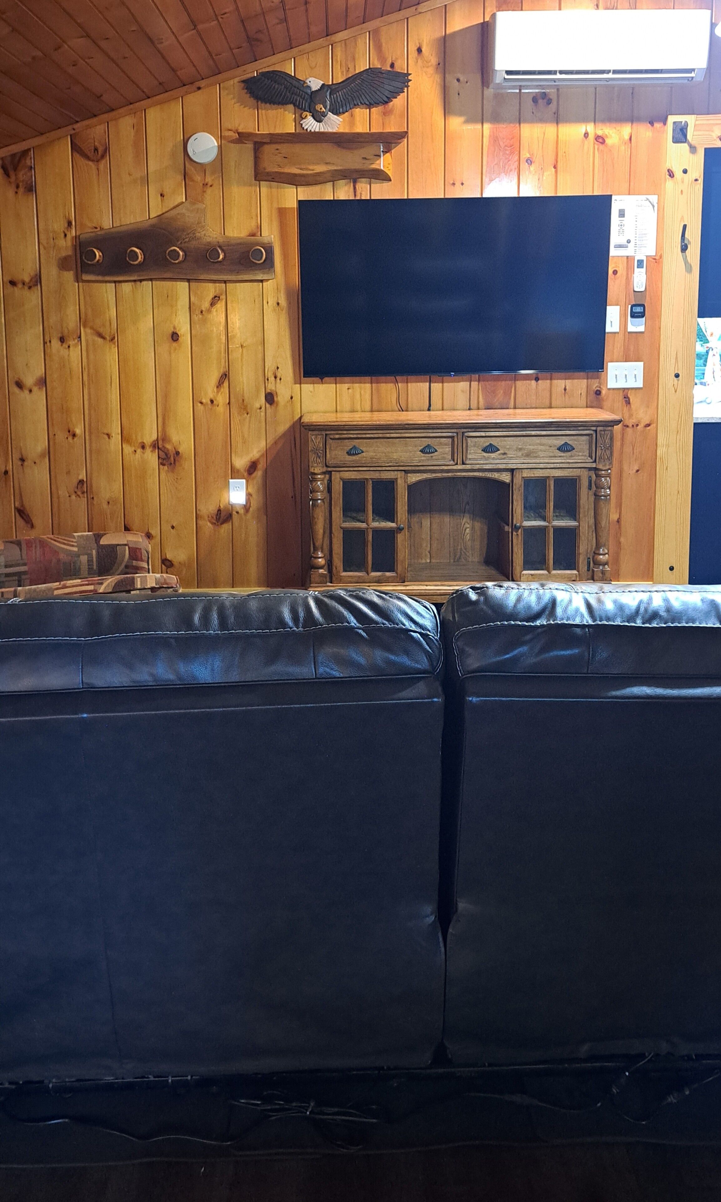 Quarto com paredes de madeira, uma decoração de águia fixada na parede, televisão de tela plana e um armário de madeira.