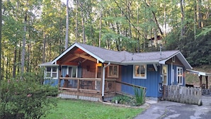 Une maison en bois à deux étages, dotée d’un porche et entourée d’une forêt.