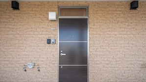 A metallic door with a keyhole and a handle, set in a brick wall with a small utility box and a water meter to the left. - CHARMANT 1D (Minamifurano)