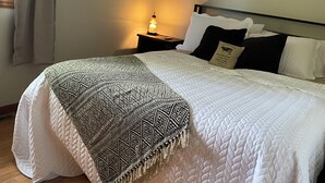 Una cama bien hecha con un plaid estampado, una lámpara de noche y un espejo en la pared.