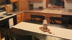 Una cocina con armarios de madera, una estufa, un microondas, una cafetera y un comedor con mesa y sillas.