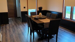 Un comedor con una mesa de madera, sillas negras y un jarrón. Se ve un ventanal con vistas a la vegetación.