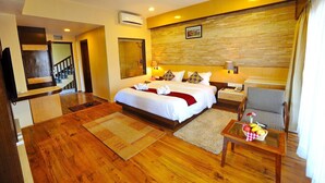 A hotel room with a large bed, a wooden floor, a small table with fruit, a chair, and a bathroom visible through an open door. - Hotel Queens Park (Pokhara)