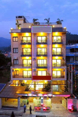 A multi-story hotel with balconies, air conditioning units, and a well-lit entrance.