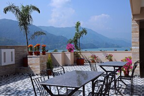 A terrace with outdoor seating, potted plants, and a view of mountains and a lake.