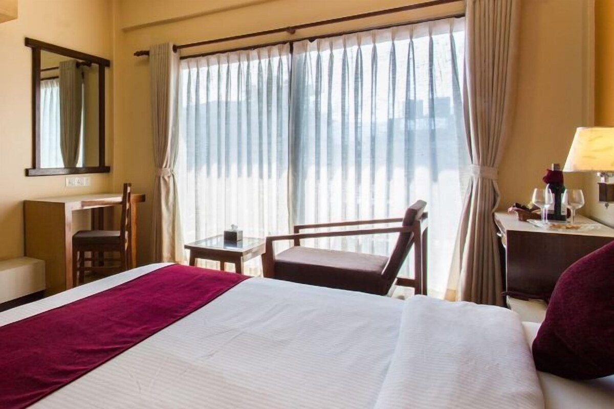 A hotel room with a bed, a desk, a chair, and a window with curtains.