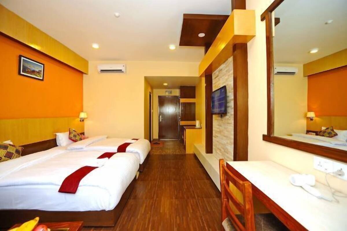A hotel room with two beds, a desk, a chair, a TV, and a large mirror.