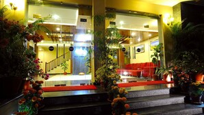 A hotel lobby with a staircase, red seating area, and multiple potted plants. - Hotel Queens Park (Pokhara)