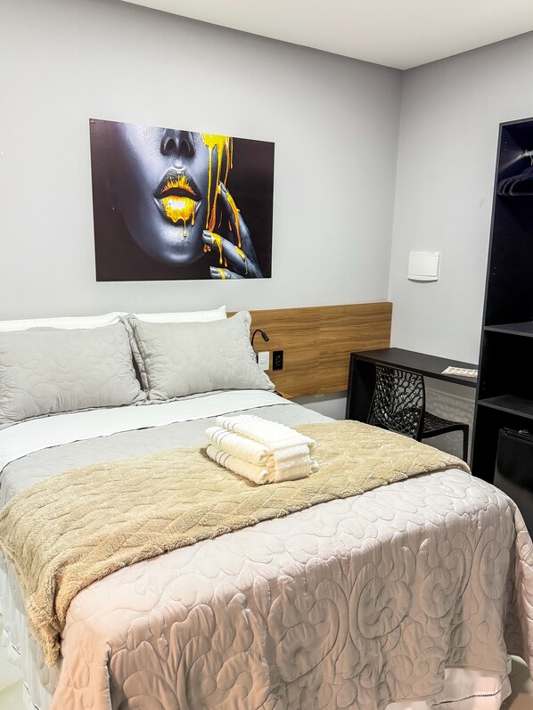 Un lit bien fait, avec une couverture et des oreillers de couleur beige, un grand tableau abstrait accroché au mur et une tête de lit en bois.