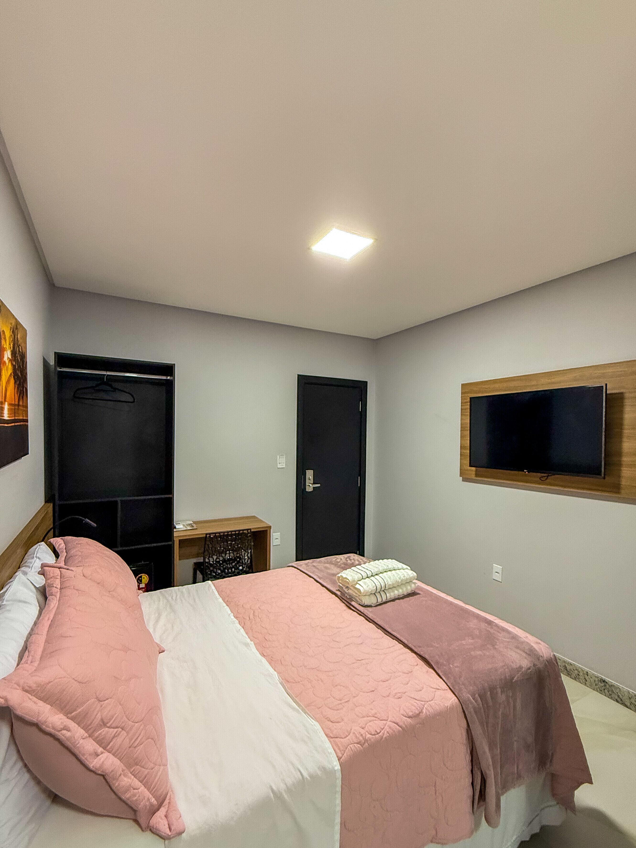 Une chambre à coucher avec un lit, un téléviseur fixé au mur, une armoire et une porte.