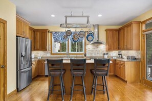Una cocina con armarios de madera, un refrigerador de acero inoxidable, una barra con taburetes y una ventana decorada con placas.