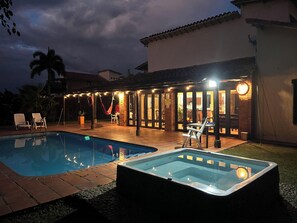 A backyard with a swimming pool, a hot tub, and a covered patio area with string lights.