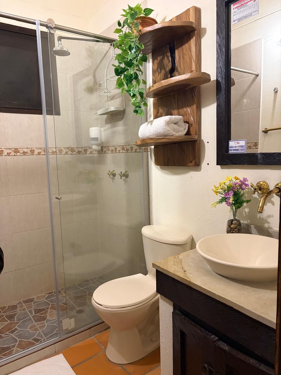 Une salle de bain avec une douche à parois de verre, des toilettes, un lavabo et des étagères en bois sur lesquelles est posée une serviette.