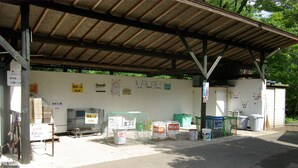 A covered outdoor area with various signs and equipment, including a metal cage, buckets, and a green net. - Gujohachimanshizenen - Bungalow (Gujo)