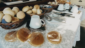 Buffet de café da manhã com diversos pães, doces e panquecas.