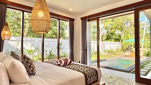 A bedroom with a large bed, two hanging lamps, and a view of a swimming pool and garden.