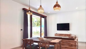 A modern dining area with a wooden table and chairs, a television mounted on the wall, and a large window with curtains.