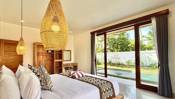 A bedroom with a large bed, wooden headboard, and two hanging light fixtures.