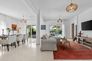 A modern living room with a sofa, dining table, and chairs, a red rug, and a pool view.
