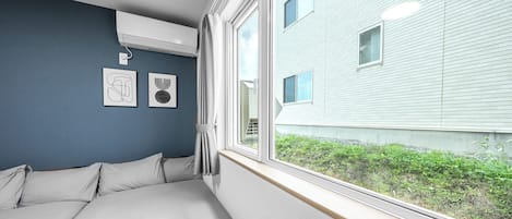 A bedroom with a large window, a bed, and two wall-mounted air conditioning units.