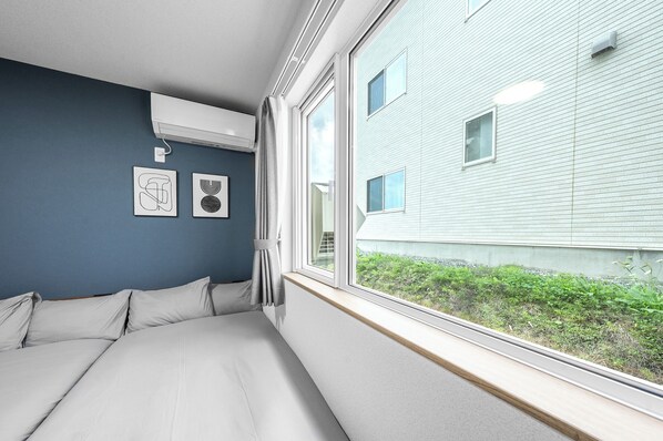 A bedroom with a large window, a bed, and two wall-mounted air conditioning units. - CHARMANT 2B (Minamifurano)