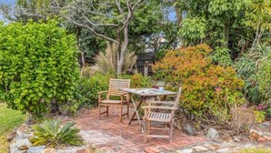 Un patio con una mesa y dos sillas, rodeado de plantas y árboles.