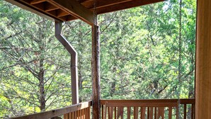 Une terrasse en bois avec un banc et une roue, entourée d’arbres.