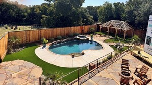 Un jardin avec une piscine, une terrasse en pierre, une terrasse en bois et une pergola.