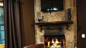Une cheminée en pierre avec un téléviseur fixé au-dessus, un fauteuil en cuir placé devant, et un plancher en bois.