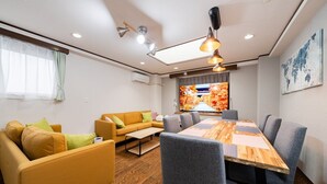 A modern living room with a sofa, a dining table, and chairs, a television, and a world map on the wall.