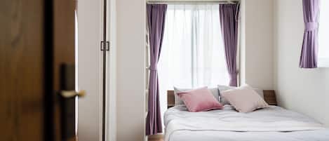 A bedroom with a bed, curtains, an air conditioning unit, and a wooden floor.