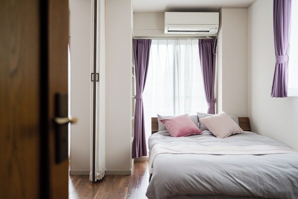 A bedroom with a bed, curtains, an air conditioning unit, and a wooden floor.