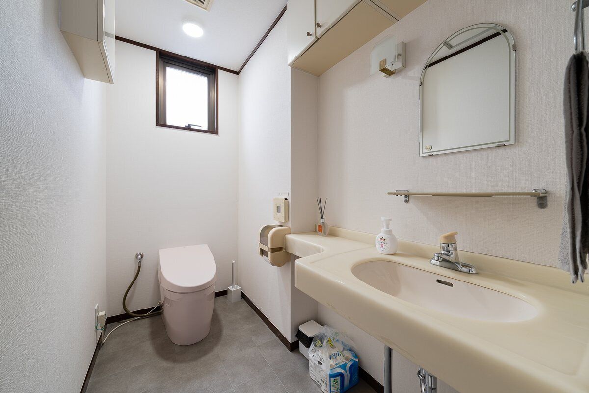 Une petite salle de bain avec des toilettes, un lavabo, un miroir et une fenêtre.