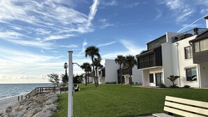 A coastal residential area with modern buildings, a grassy lawn, a bench, and a paved walkway by the sea. - Tamarind – 2BR Condo with Lemon Bay Views (Englewood)