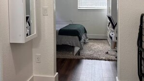 A narrow hallway leading to a bedroom with a bed, a dresser, and a chandelier. - Cozy Suburb Studio (Everett)