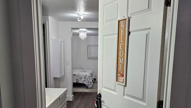A hallway leading to a bedroom with a bed, a chandelier, and a welcome sign. - Cozy Suburb Studio (Everett)