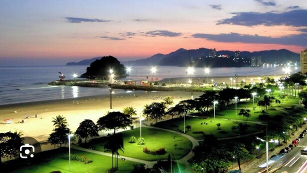 A coastal cityscape at dusk with a beach, illuminated street lights, and distant mountains. - Beautiful beachfront apartment in a prime location in Santos for you and your pet. (Santos)