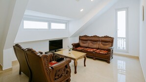 Una habitación amplia con techo alto, un ventanal grande, un televisor de pantalla plana, un sofá de madera y una mesa de comedor.