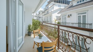 Un balcón con una mesa y sillas, una planta en maceta y vistas de edificios cercanos.