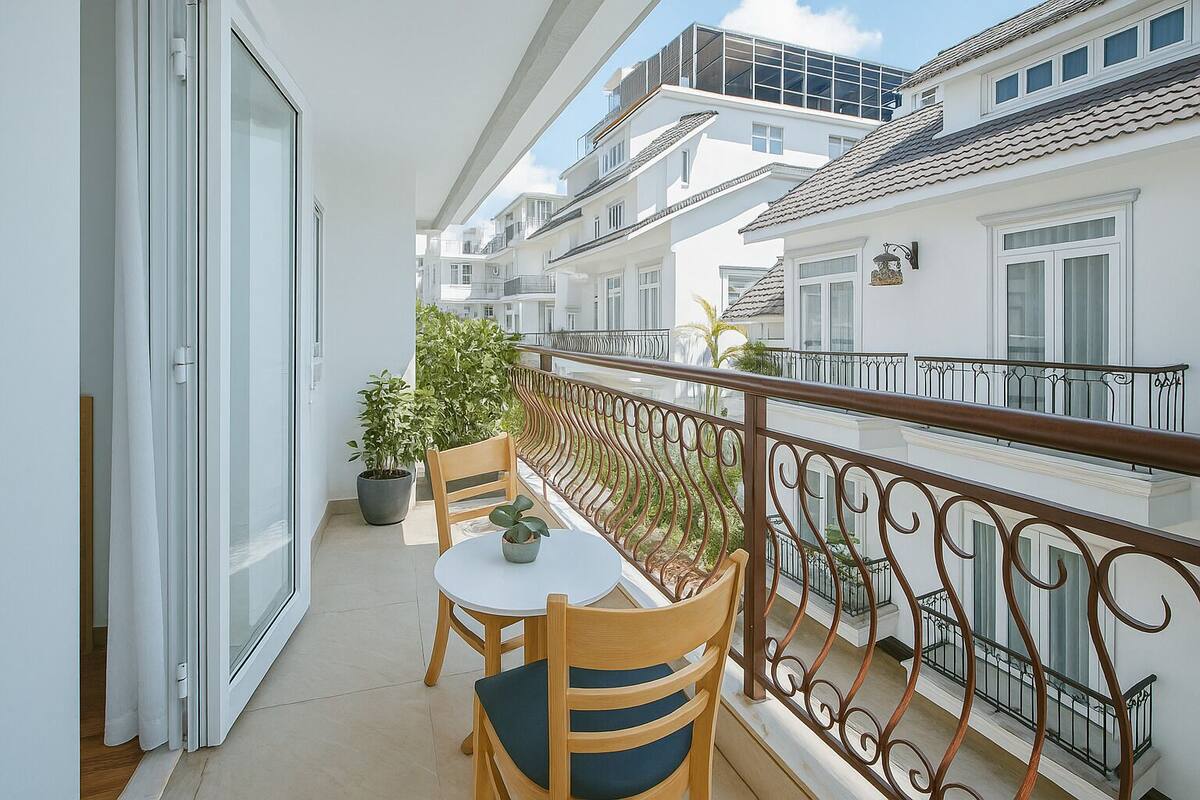 A balcony with a table and chairs, a potted plant, and a view of neighboring buildings.