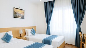 Habitación de hotel con dos camas, piso de madera, un escritorio y un ventanal con cortinas azules.