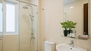Un baño moderno con cabina de ducha de vidrio, inodoro, lavamanos y espejo.