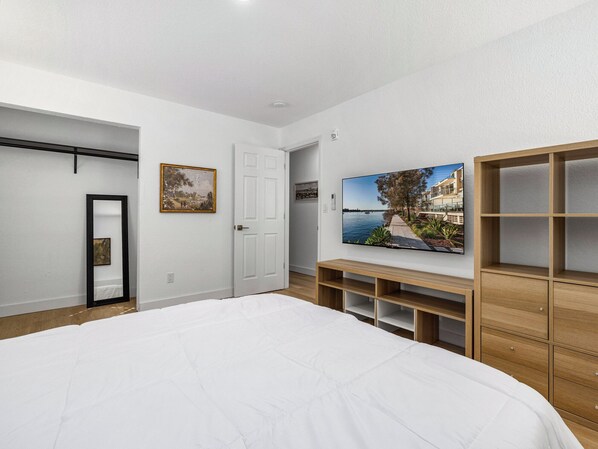 Un dormitorio con una cama grande, un televisor montado en la pared, una puerta y un armario de madera.