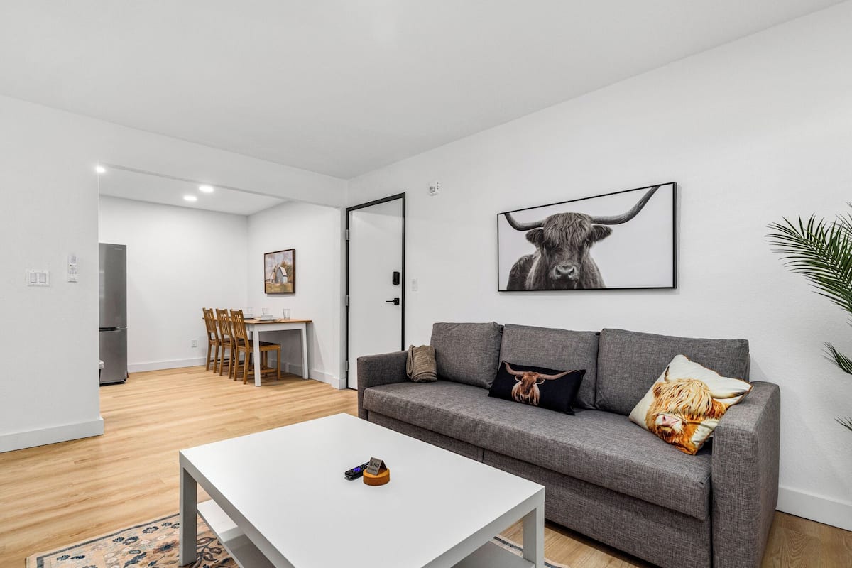 Un salon moderne avec un canapé gris, une table basse blanche et un coin repas comprenant des chaises et une table en bois.