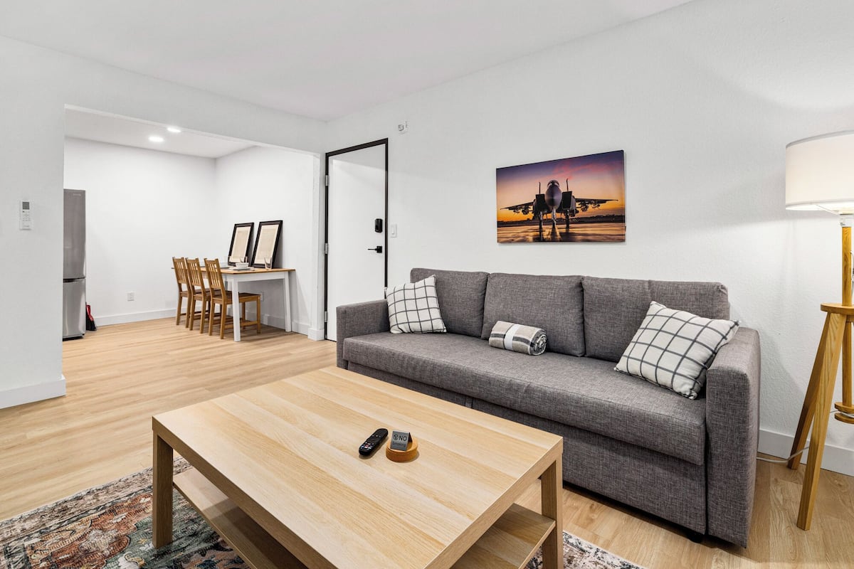 Un salon moderne avec un canapé gris, une table basse en bois et un tableau représentant un avion accroché au mur.