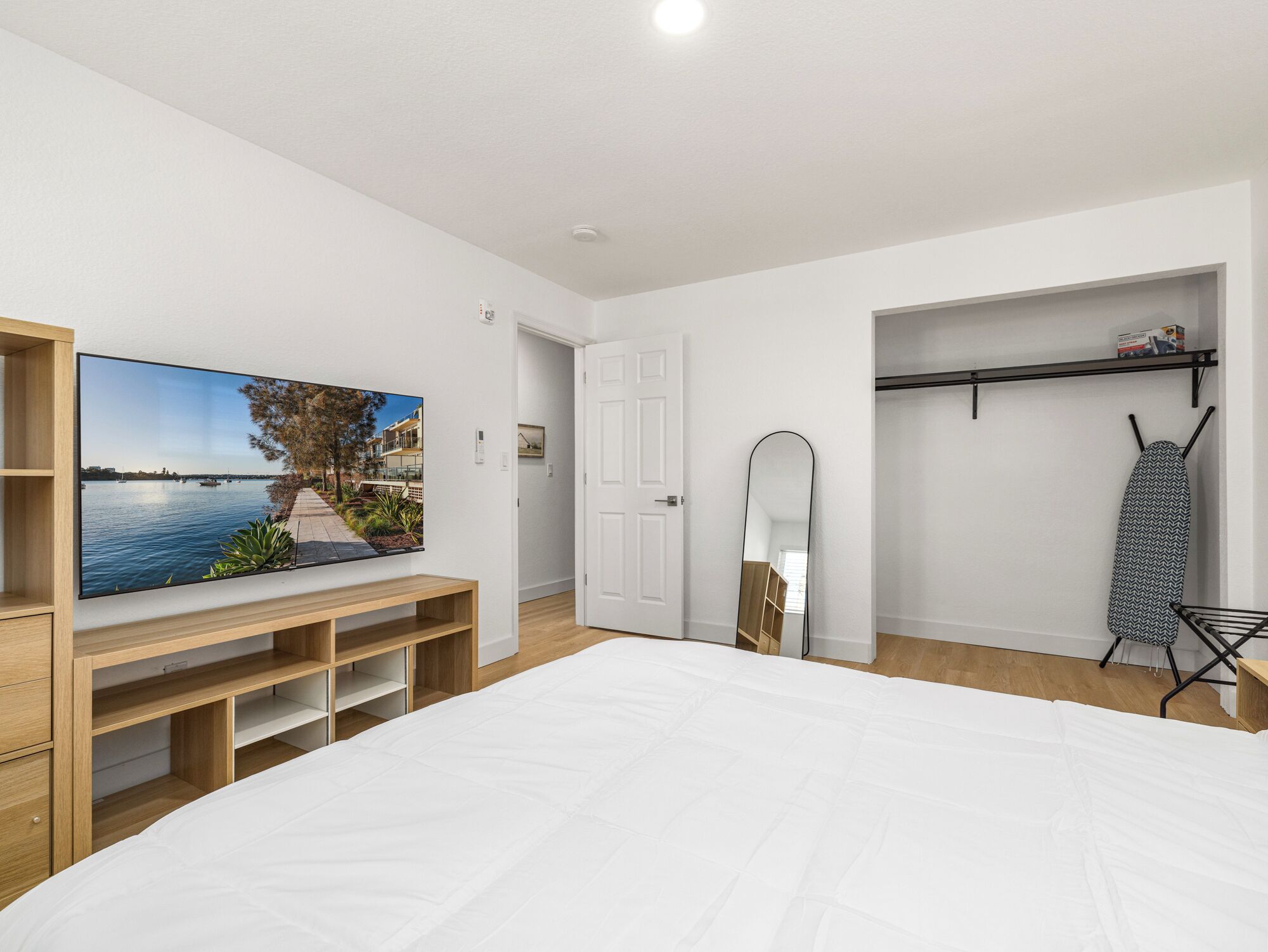 Un dormitorio con una cama grande, un televisor montado en la pared, un armario y una puerta que da a otra habitación.