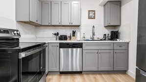 A modern kitchen with grey cabinets, stainless steel appliances, and a wooden floor. - Casitas en Pueblo - Central Lofts (Pueblo)