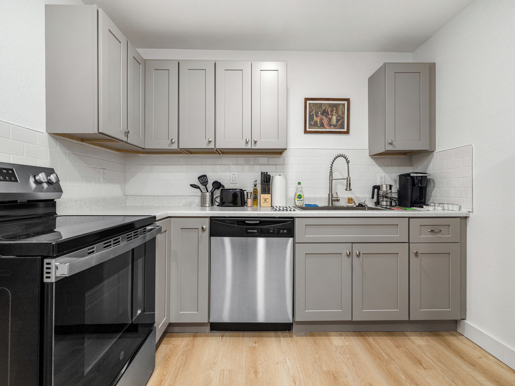 Una cocina moderna con gabinetes grises, un lavavajillas de acero inoxidable, un horno integrado y una cafetera.
