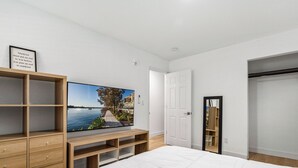 A bedroom with a large bed, wooden shelving, a TV, and a door leading to another room. - Casitas en Pueblo - Central Lofts (Pueblo)