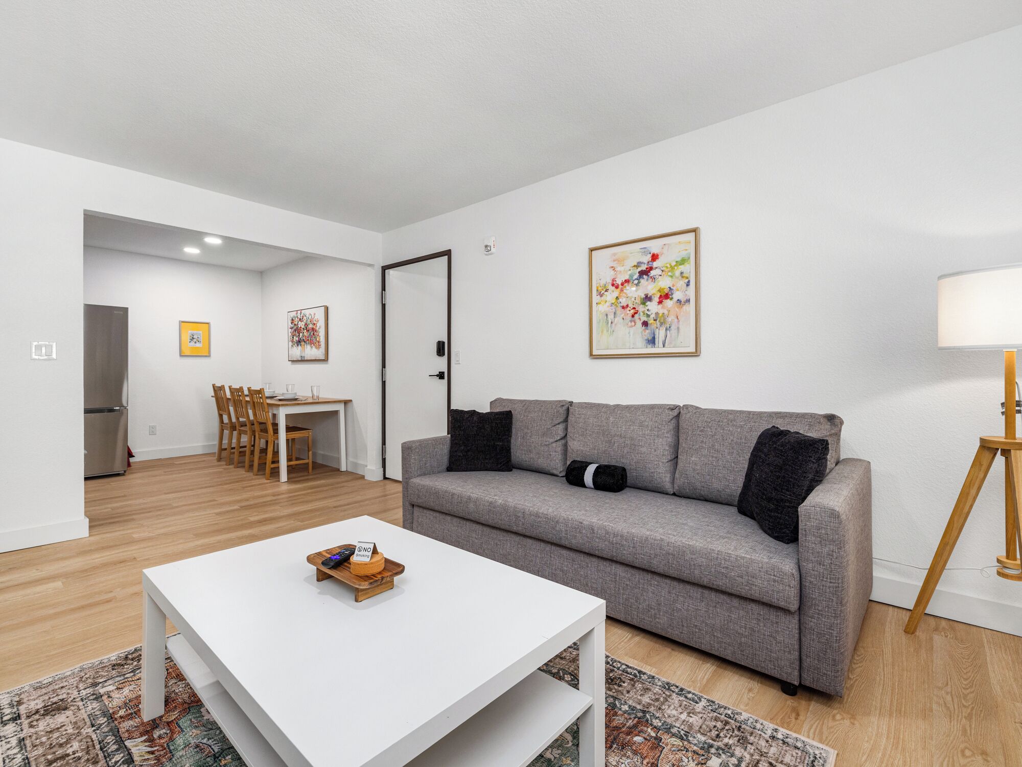 Een moderne woonkamer met een grijze bank, een witte salontafel en een eethoek met houten stoelen.
